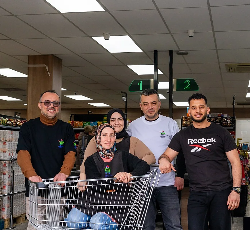 Het team van Unique Supermarkt met een winkelwagen in de winkel